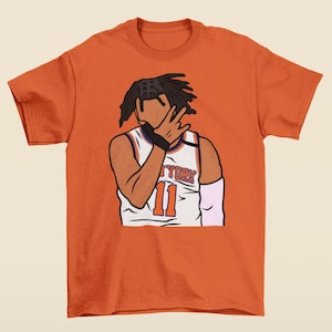 May include: Orange t-shirt with a cartoon illustration of a basketball player wearing a white jersey with the text "New York" and the number "11" on the front.