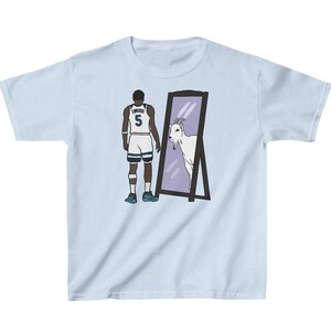 Pode incluir: Uma camiseta azul claro com um gráfico de um jogador de basquete olhando para um espelho e vendo uma cabra. O jogador está vestindo uma camisa branca e azul com o número 5. O texto "DONCIC" está na parte de trás da camisa.