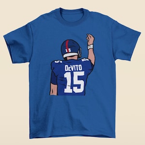 May include: A royal blue t-shirt with a cartoon illustration of a football player wearing a blue and red helmet with the number 15 on it. The player is wearing a blue jersey with the name "DeVito" and the number 15 on the back. The player is raising his right arm in the air.