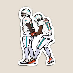 May include: Two football players in white and teal uniforms, one holding the other's hand. The player in the front has the number 11 on their jersey and the text "Waddle" above it.