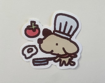 Könnte beinhalten: Aufkleber mit einem Cartoon-Kochhund, der eine weiße Kochmütze und ein rotes Halstuch trägt. Der Hund hält eine Bratpfanne. Eine Tomate und ein Spiegelei sind ebenfalls enthalten.