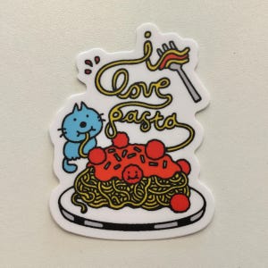 Puede incluir: Una pegatina troquelada que muestra un gato azul comiendo espaguetis de un plato blanco con salsa roja y albóndigas. El texto "I love pasta" está escrito en cursiva amarilla sobre el plato, junto a una ilustración de un tenedor.