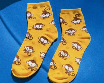 May include: A pair of yellow socks with a repeating pattern of cartoon monkeys. The monkeys have brown faces and white accents. The socks are on a blue surface.