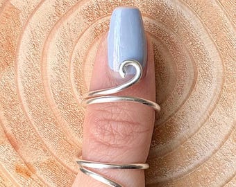 May include: Silver thumb ring with a spiral design. The ring is wrapped around the thumb and has a curved end.