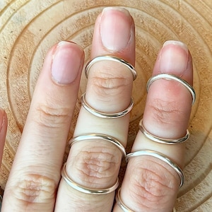 May include: A set of five silver rings stacked on a finger. The rings are all different sizes and are made of a smooth, shiny metal.