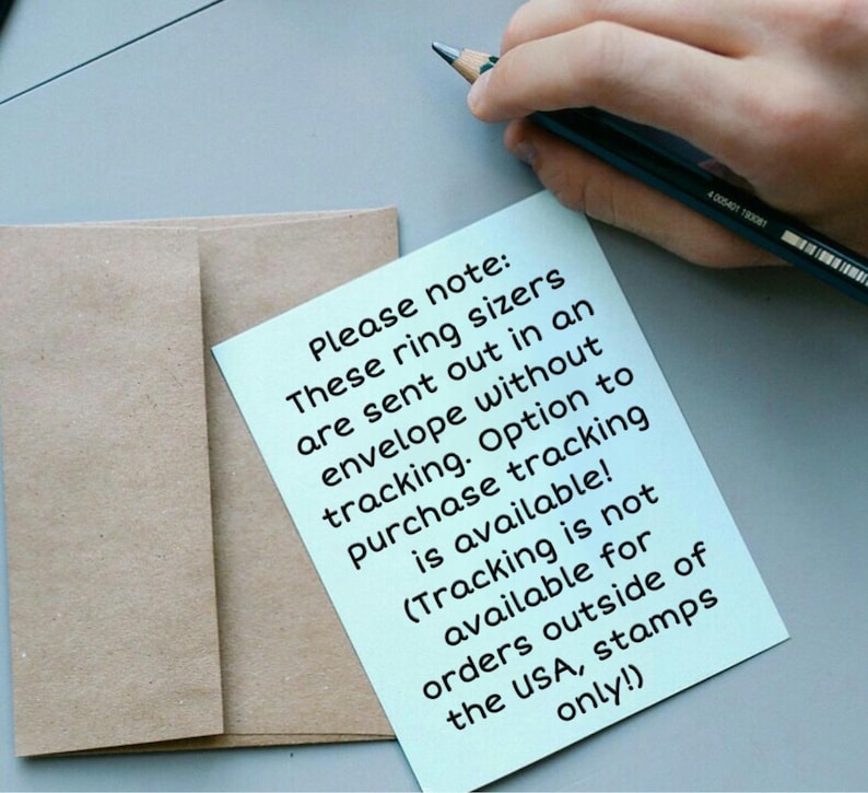 May include: A light blue sticky note with text about ring sizers and shipping information, next to a brown envelope. A hand holds a pencil in the upper right corner. The text on the note reads: "Please note: These ring sizers are sent out in an envelope without tracking."