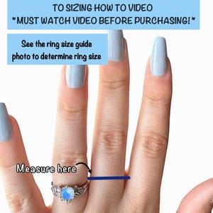 May include: A silver ring with a blue gemstone is worn on a finger. The image includes text that says "Measure here" and instructions to see the description for a sizing video and ring size guide. The ring has a decorative design.