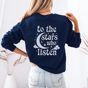 Può includere: Felpa blu navy con la scritta bianca "to the stars who listen". Il design include una luna crescente, stelle e nuvole. La felpa è a girocollo e maniche lunghe.
