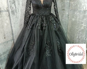 May include: A black tulle ball gown with long sleeves and a V-neckline. The gown is adorned with black lace and sequins. The gown is on a mannequin and the background is a gray wall. The text "OllyBridal!" is in a wreath on the bottom right of the image.