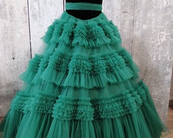May include: A strapless green tulle ball gown with a black velvet bodice and a green satin sash. The skirt is layered with ruffles and has a full, flowing silhouette.