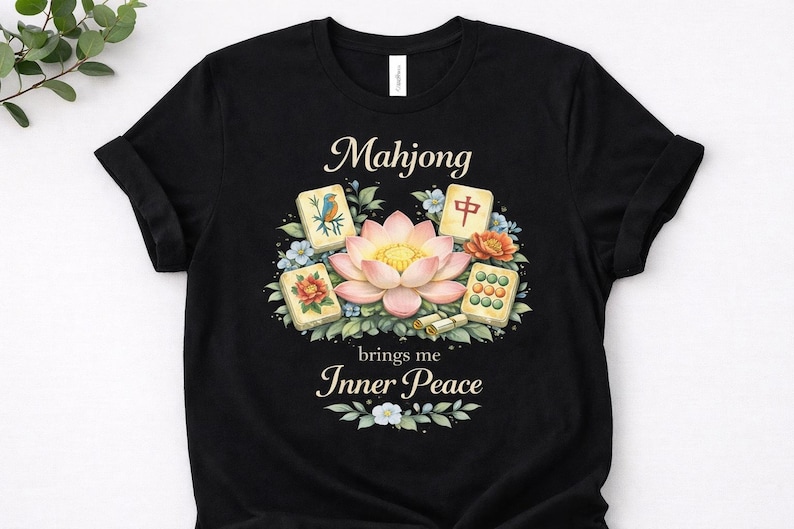 May include: Black t-shirt with a watercolour design featuring the word "Mahjong" above a lotus flower and Mahjong tiles. The text "brings me Inner Peace" is below the design. The design includes blue and orange floral accents.