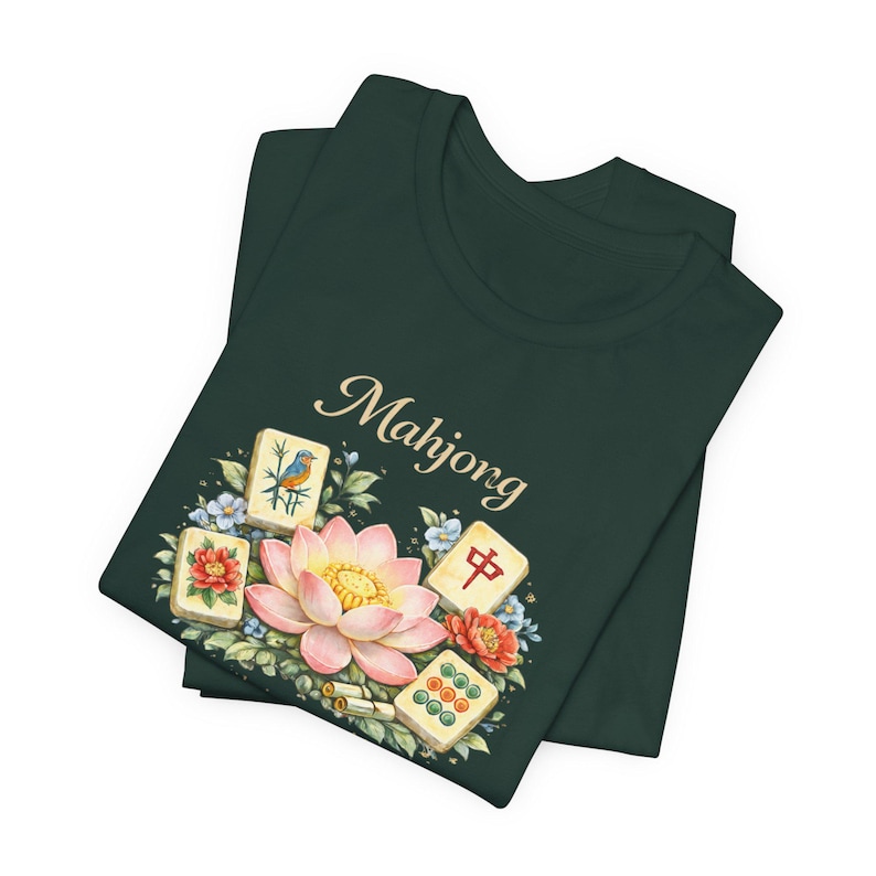 May include: Dark green t-shirt with a floral and Mahjong tile design. The design includes a pink lotus flower, blue and red flowers, and several Mahjong tiles. The word "Mahjong" is written in a cursive font.