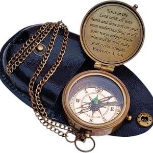 May include: A vintage brass compass with a protective leather case and chain. The compass features a glass cover, a needle, and directional markings. The lid of the compass has an engraved Bible verse. The compass is open, revealing the internal workings.