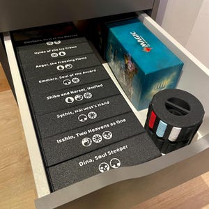 May include: A drawer filled with Magic: The Gathering card game accessories. Includes black card storage boxes with white text, a teal box with the word "MAGIC", and a black and multi-colored token holder.