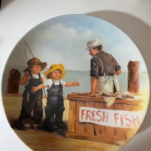 May include: A vintage ceramic plate with a painting of two children selling fresh fish to a man. The plate has a blue sky, a wooden dock, and a sign that says "Fresh Fish". The artist's signature, "Jeanne Down", is in the bottom right corner.