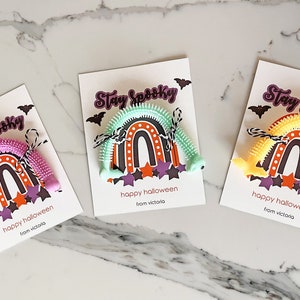 May include: Three Halloween-themed cards with the text "Stay Spooky" printed on each. Each card features a rainbow-shaped toy with a different color: pink, green, and yellow. The text "happy halloween from victoria" is printed on each card.