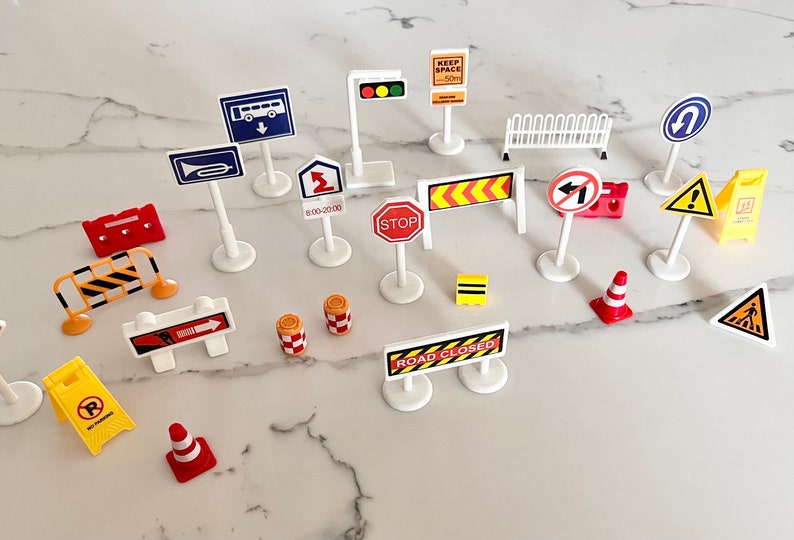 May include: A collection of miniature road signs and traffic cones, including signs for 'Keep Space 50m', 'Stop', 'Road Closed', 'No Entry', and 'Bus Lane'.