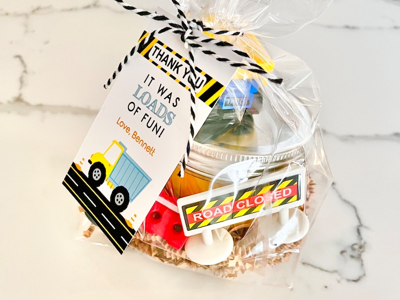 May include: A yellow and black construction themed party favor bag with a thank you tag that reads "It was loads of fun! Love, Bennett". The bag contains a small jar with a yellow lid, a road closed sign, and other construction themed toys.