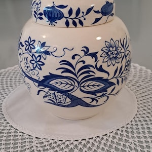 May include: A white ceramic jar with a blue and white floral design. The jar has a lid and is decorated with a repeating pattern of flowers and leaves.