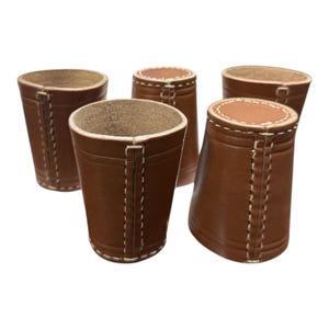 Può includere: Cinque bicchieri da dado in pelle marrone con cuciture bianche. I bicchieri sono tutti della stessa dimensione e forma, e sono disposti in fila.