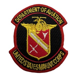 Op de afbeelding: Een geborduurde patch in rood, wit en goud met de tekst "Department of Aviation United States Marine Corps". De patch toont een gestileerde adelaar met een schild en een propeller.