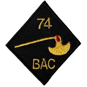 May include: Black diamond-shaped patch with gold embroidered text "74 BAC" and a gold embroidered axe with a red handle.