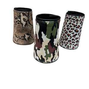 May include: Three beverage can coolers with different patterns. One has a snakeskin print, another has a camouflage pattern in green, brown, and beige, and the third has a leopard print in red and black.