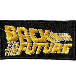 Pode incluir: Um remendo de tecido preto com texto bordado em amarelo que diz "De volta para o futuro".