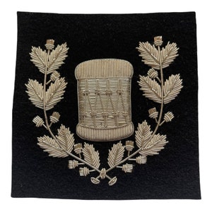 May include: A silver embroidered patch on a black background. The patch features a drum with a wreath of leaves around it.