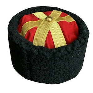 May include: A black fur hat with a red crown and gold trim. The crown has a gold button in the centre.