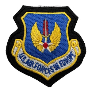 May include: A blue and yellow embroidered patch with the text "US Air Forces in Europe" and a stylised eagle with wings spread.
