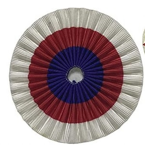 Könnte beinhalten: Eine weiße, rote und blaue Rosette mit einem Loch in der Mitte. Die Rosette ist aus gefaltetem Stoff.