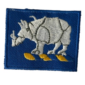 May include: A blue embroidered patch with a white rhinoceros standing on two yellow waves.