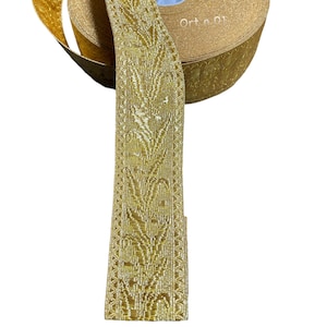 Pode incluir: Bordado dourado com padrão floral. O bordado está enrolado em um carretel. O carretel tem o texto "Ort n 01" impresso nele.