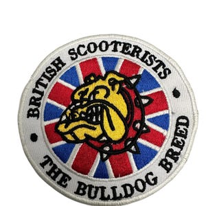 Può includere: Toppa rotonda ricamata con un bulldog giallo e nero su sfondo rosso, bianco e blu. I testi "BRITISH SCOOTERISTS" e "THE BULLDOG BREED" sono ricamati in cerchio.