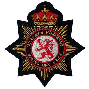 May include: A black embroidered patch with a gold starburst design. The center of the patch features a red lion on a white circle with the text "Murray's Regiment Pipes and Drums" around the circle. A gold crown is above the circle.