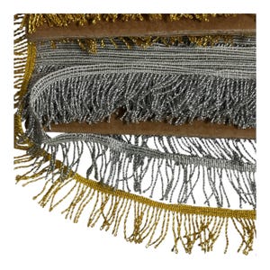 May include: Close-up of decorative fringe trim in gold and silver. The fringe is made of metallic threads and is attached to a brown backing. The trim is layered, showing different styles and colours.
