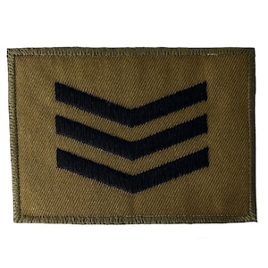 May include: A brown fabric patch with three black chevrons. The patch is edged with a green border.
