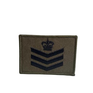 May include: Olive green rectangular patch with three black chevrons and a black crown emblem. The patch has a stitched border and is likely a military or service rank insignia.