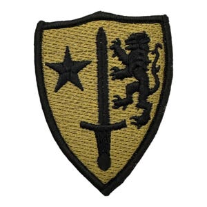 Könnte beinhalten: Ein gestickter schwarzer und brauner Aufnäher in Form eines Schildes. Der Schild zeigt einen schwarzen Stern, ein Schwert und einen Löwen.