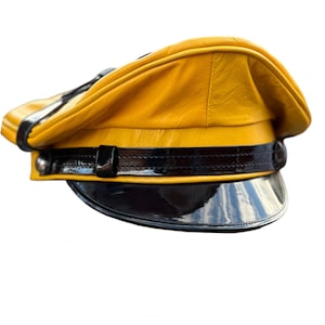 Peut inclure: Une casquette en cuir jaune avec une visière en cuir verni noir et une bande noire autour de la couronne.