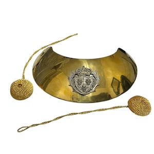 May include: A gold-colored metal collar with a silver-colored crest featuring a crown and three stylized leaves. The collar is attached to two gold-colored cords with tassel ends.