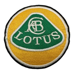 Può includere: Una toppa ricamata con il logo Lotus. Il logo è un triangolo verde con la parola "LOTUS" in lettere bianche e un cerchio bianco che contiene le lettere "A" e "B" al suo interno.