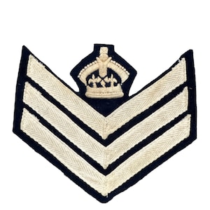 May include: A black fabric chevron with three white stripes and a gold embroidered crown on top.