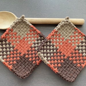 Könnte beinhalten: Zwei gewebte Topflappen in Braun, Orange und Beige mit einem Nudelholz im Hintergrund.