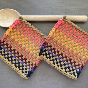 May include: Two woven pot holders in a rainbow of colors, including pink, orange, yellow, brown, purple, and blue. The pot holders have a braided border.