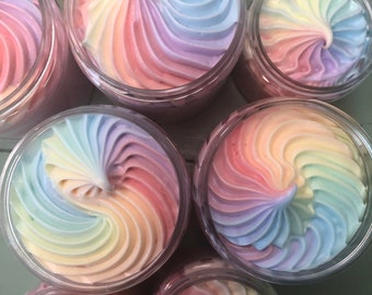 May include: Six jars of whipped body butter with a rainbow swirl design. The jars are clear plastic and the body butter is a light pink, yellow, and blue color.