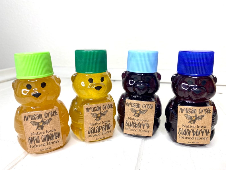 May include: Four small bear-shaped bottles of honey, each with a different flavor: apple cinnamon, jalape&ntilde;o, blueberry, and elderberry. Each bottle has a brown label with the text "Artisan Creek" and the flavor of the honey.