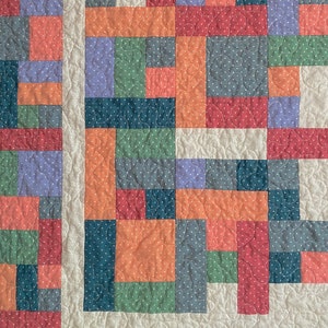 Op de afbeelding: Een patchworkdeken met een verscheidenheid aan kleuren en patronen, waaronder rood, oranje, groen, blauw en paars. De deken is gemaakt van vierkanten en rechthoeken, en de naden zijn zichtbaar. De deken is gestikt met een eenvoudig steekpatroon.