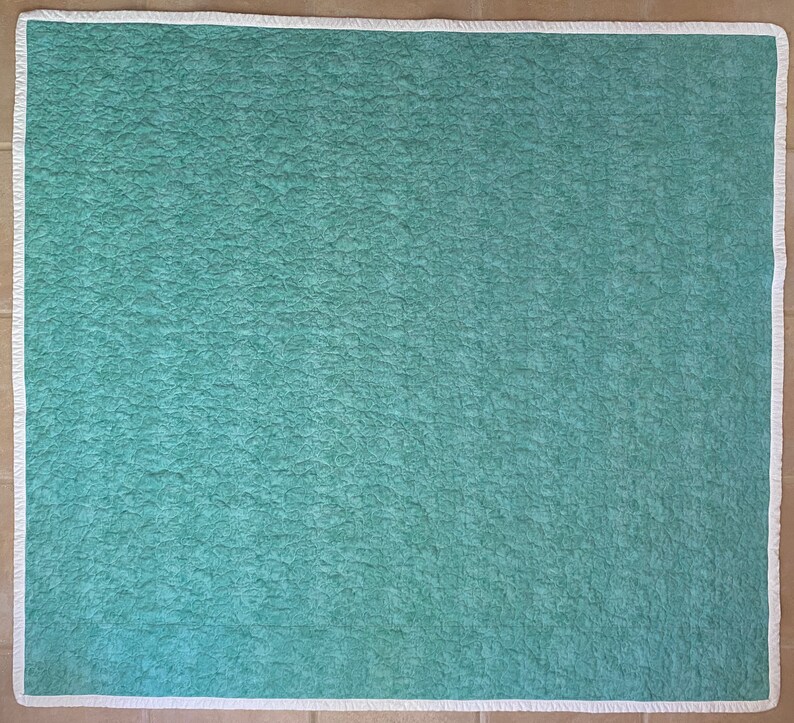 Op de afbeelding: Een tealblauwe quilted stof met een witte rand.